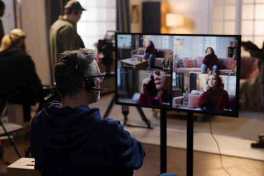 A male director monitors an actress on screen during production