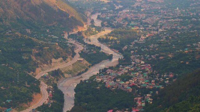 4K shot of River Beas flowing besides the Chandigarh Manali Highway and Kullu city as seen from above the nearby mountain during the sunset in Himachal Pradesh, India. Scenic view of Kullu at dusk. 