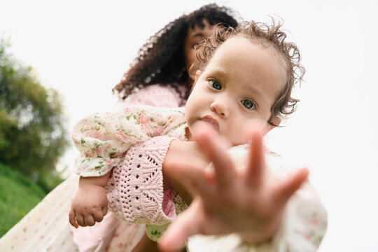 A mother holds her baby reaching towards the camera outdoors
