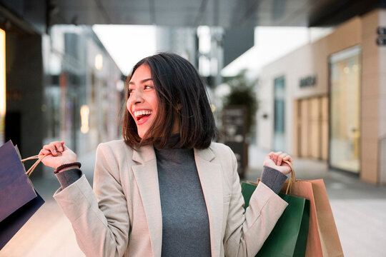 Happy consumer holding shopping bags outdoors in modern city