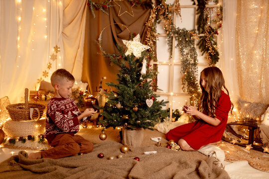 Child siblings decorating a Christmas tree in a cozy room