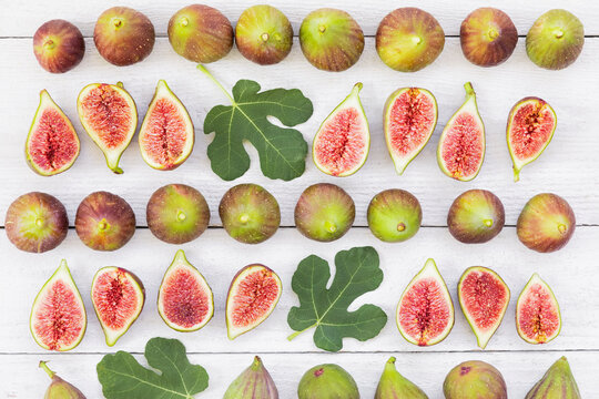 Fresh whole and halved figs arranged in rows on a wooden table