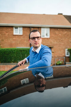 Man wearing eyeglasses stands by his car in a residential area