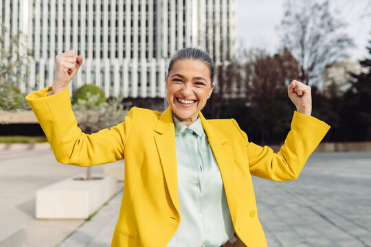 Cheerful businesswoman flexing muscles at office park on sunny day