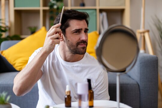 Man grooming hair in living room with mirror and cosmetic products
