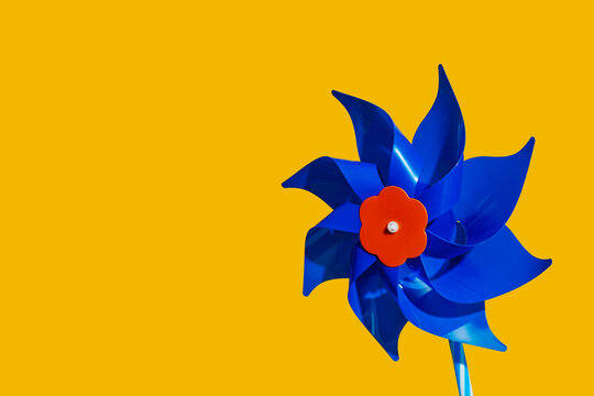 A blue plastic pinwheel toy stands against a bright yellow background