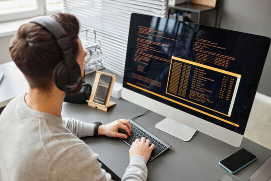 Young computer programmer wearing wireless headphones coding on computer