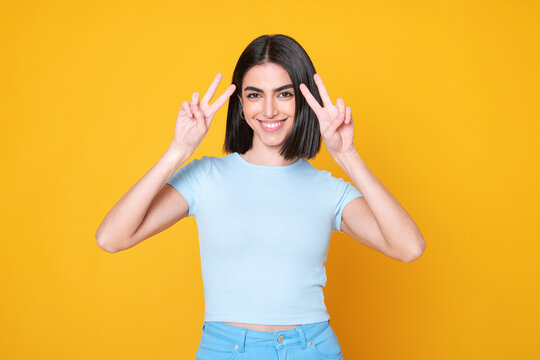 Smiling young woman gesturing peace sign against yellow background
