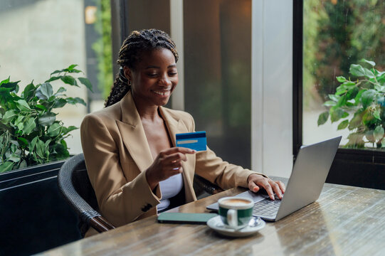 Happy businesswoman holding card in front of laptop at cafeteria
