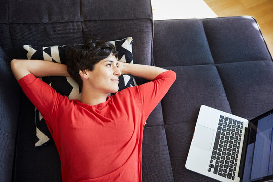 Woman lying on couch at home next to laptop