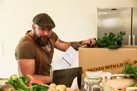 Mature man with delivery service packing organic vegetables in cardboard