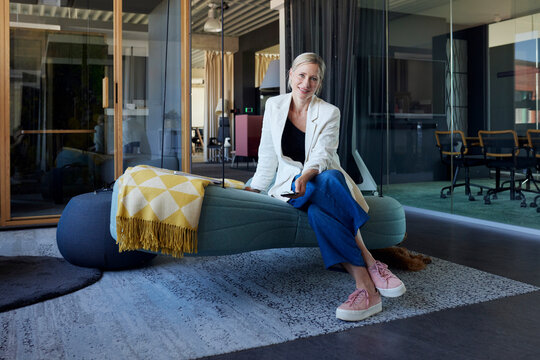 Smiling businesswoman sits on an office swing holding a smartphone