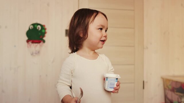 Little girl holding a yogurt cup and spoon after enjoying a healthy snack at home