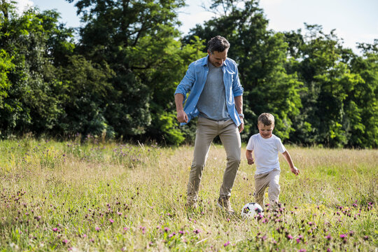 Father and son playing soccer in a sunny meadow