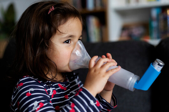 Close-up of asthmatic girl using inhaler in living room at home