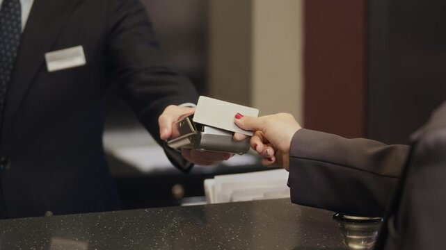 Customer tapping blank card on payment terminal held by receptionist at hotel front desk. Perfect for illustrating contactless payment, modern hospitality services and secure transactions, Close Up