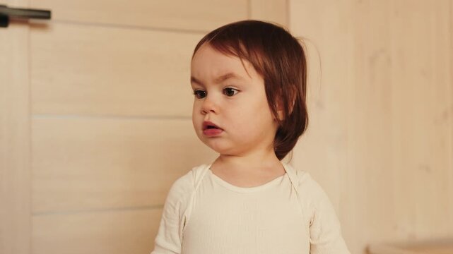 Curious 3 year old girl looking at camera with thoughtful expression inside a cozy wooden home