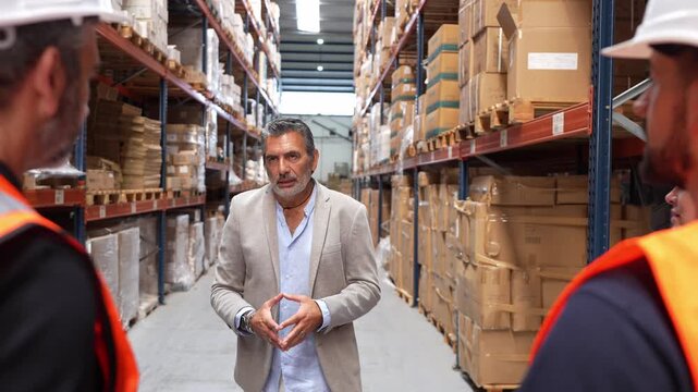 Logistics manager talking to a diverse team of employees in a large distribution center aisle. The supervisor is explaining order fulfillment