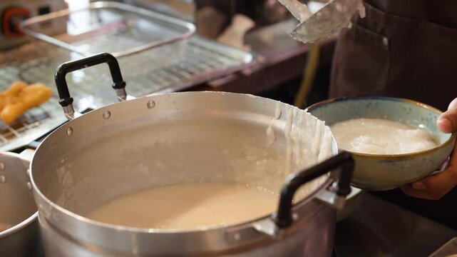 Chef Serving Hot Asian Rice Porridge from Large Metal Pot