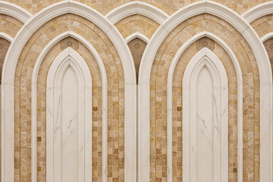White marble and tan stone wall with layered arched niches, architectural interior detail featuring repeating stone masonry and curved frames