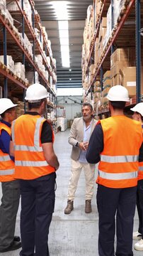 Logistics manager talking to a diverse group of male and female warehouse employees during a daily briefing inside a distribution center