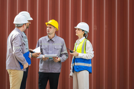 Diverse group of industrial workers and engineers in hard hats meeting in cargo shipping containers, Industrial site managers and construction team talking and planning work at container yard