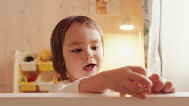 Curious 3 year old girl playing with small toys on a table inside a cozy wooden home