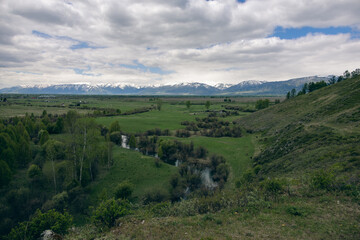 Fototapeta premium Panoramic view of green valley with winding river and snowy mountains in background