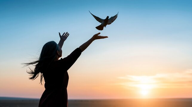 Woman silhouette releasing dove into evening sky, symbolizing freedom, hope, and new beginnings at sunset