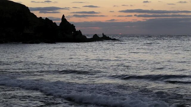 Sun beginning to rise beside solitary fisherman on rocky Gran Canaria coast