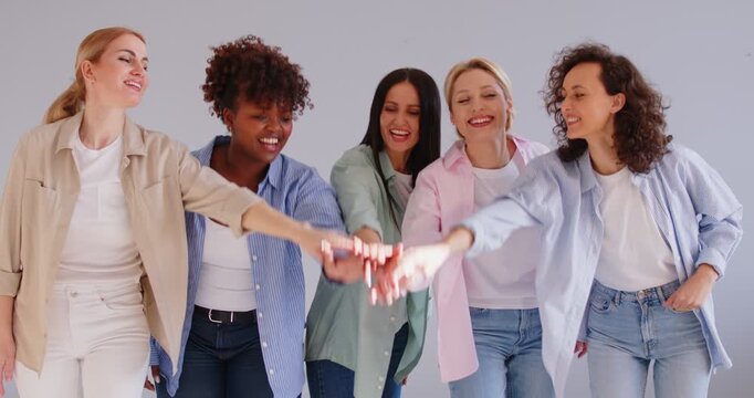 Group of happy young women standing together in row, stacking hands in gesture of unity and teamwork. Cheerful female friends in casual clothes celebrating success, showing collaboration and support.