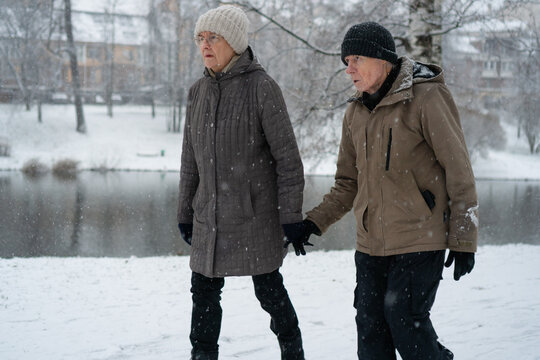 Senior couple walking hand in hand in a snowy winter wonderland with happy faces. Elderly pair strolling in warm coats enjoying a joyful moment. Content companions sharing a cheerful walk in the snow