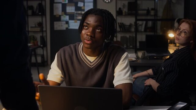 Medium shot of African American young adult man discussing project with Caucasian young adult female colleague in office at night. Video ideal for corporate communication and teamwork marketing
