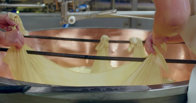 Slow Motion Of Dairy workers stretching long sheets of elastic cheese curd across metal rods during traditional production. Cheesemakers Stretching Elastic Curd over Copper Vat