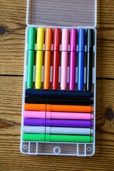 Fototapeta premium Set of assorted colorful marker pens are neatly arranged in a clear plastic case on a rustic wooden table. These art supplies are ready for creative projects for hobbyists and artists.