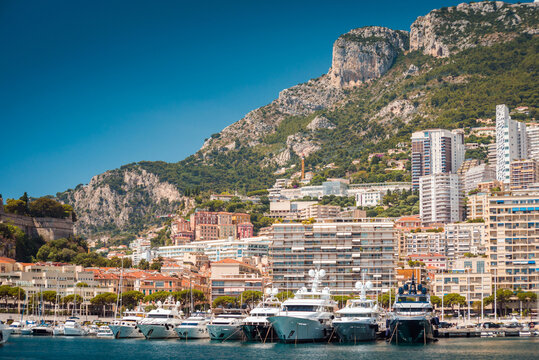 The port of Hercules in Monte Carlo, Monaco on a sunny summer day, with blue sky, beautiful mountain and cityscape  and lots of super yachts docked in the marina