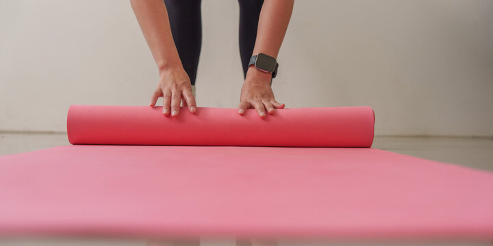 Cropped hands rolling pink yoga mat on floor for fitness routine