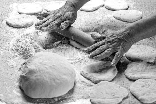 Woman rolling out dough on kitchen table, closeup. Black and white