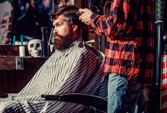 Man visiting hairstylist in barbershop. Barber works with hair clipper. Hipster client getting haircut