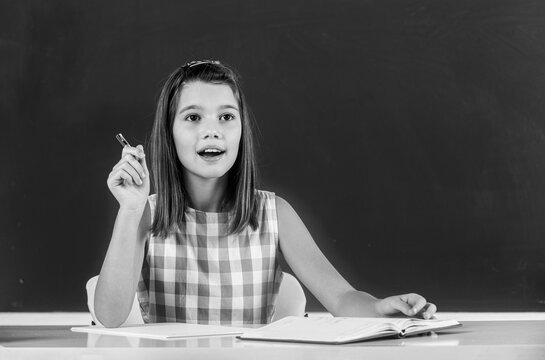 The student writes in a notebook. Cute girl sits in a classroom at a table with notebooks and textbooks. Black and white