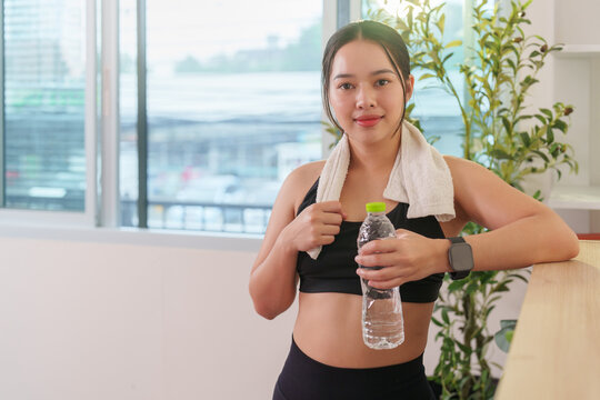Smiling Asian woman holding water bottle after workout for hydration and wellness