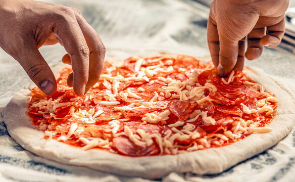 Cook hand makes a pizza, puts the sausage on top. Hand sprinkling cheese on pizza dough with tomato sauce