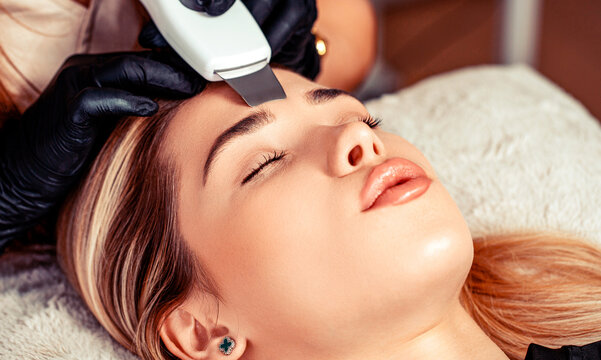 Beauty doctor ultrasonic scrubber doing procedure of ultrasonic cleaning of face. Cosmetology, facial skin care. Closeup