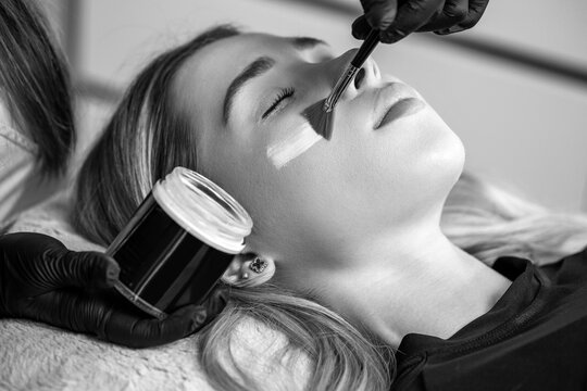 Woman getting a facial mask treatment at the beauty salon. Facial skin care procedures. Black and white