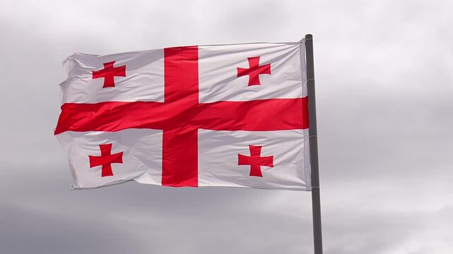 Georgian national flag, known as the five cross flag, waving proudly on a flagpole against a dramatic gray and cloudy sky, symbolizing the country's patriotism and national identity slow motion