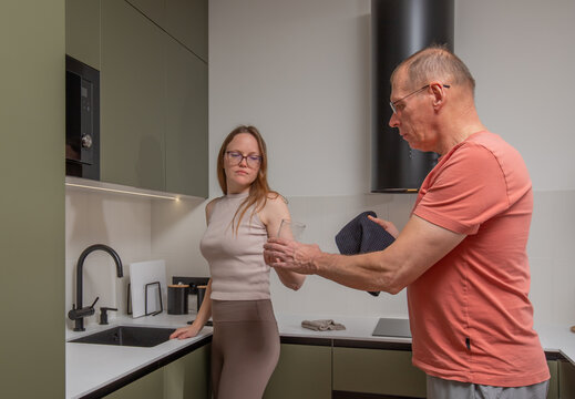 Woman washing dishes hands glass to husband. Couple sharing kitchen cleanup task at home together.