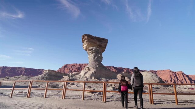 Mother and daughter walk towards railing around El Hongo rock formation in Ischigualasto Provincial Park