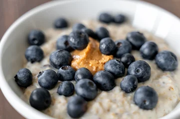 Bowl of oatmeal porridge with blueberries and peanut butter on wooden table, healthy breakfast and nutrition © molenira