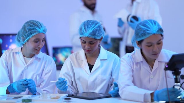 Three scientists examine sample dishes together at a microscope bench, concentrating under the blue glow of a modern research lab.