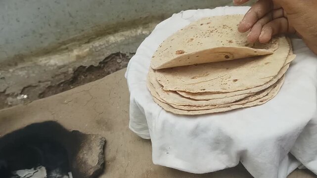 Homemade Indian roti stacked neatly on cloth. Clay background visible. Perfect for content about Indian food, village life and traditional culinary practices.